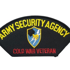 May include: A black embroidered patch with a curved top edge. The text ARMY SECURITY AGENCY is stitched in yellow at the top, and COLD WAR VETERAN is in red at the bottom. A central shield features a blue background with a yellow lightning bolt.