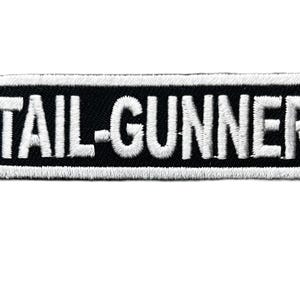 May include: A rectangular embroidered patch with a black background and a white border. The text TAIL-GUNNER is stitched in white capital letters across the center of the patch. The design features a clean, bold font with a visible fabric texture.