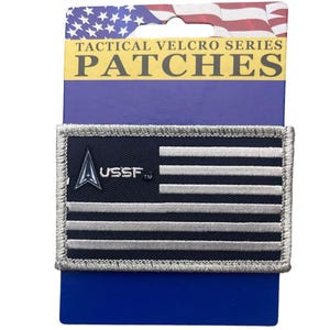 May include: A rectangular tactical patch featuring a dark blue background with horizontal silver stripes and the USSF logo in silver. The patch is mounted on a blue display card labeled TACTICAL VELCRO SERIES PATCHES with a US flag graphic.