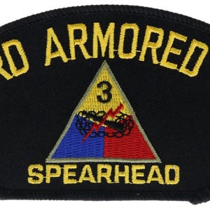 May include: A black embroidered patch featuring the text THIRD ARMORED DIV in yellow at the top and SPEARHEAD in yellow at the bottom. A central triangle contains the number 3, a red lightning bolt, and a black tank tread on a blue and red field.