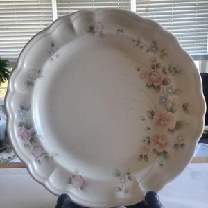 May include: A white ceramic dinner plate with a scalloped edge and a floral design featuring pink, blue, and green flowers.