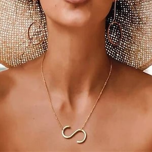 May include: A woman wearing a straw hat, round sunglasses, and a gold necklace with a letter 'S' pendant.