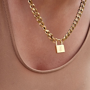 May include: A gold chain necklace with a padlock pendant. The padlock has the letter "J" engraved on it.