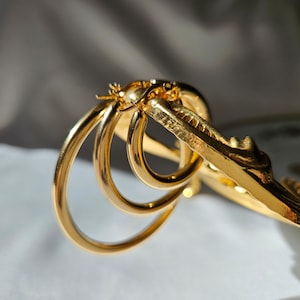 May include: Gold hoop earrings with a layered design. The earrings are stacked on top of each other, creating a unique and stylish look.