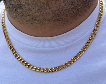 Könnte beinhalten: Eine goldfarbene Panzerkettenhalskette. Die Halskette besteht aus ineinandergreifenden Gliedern und wird um den Hals getragen. Die Person trägt ein weißes T-Shirt.