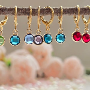 May include: A set of ten gold hoop earrings with dangling crystal charms. The charms are in various colors, including green, blue, purple, and red.