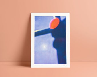 May include: A close-up of a photograph of a red circle with a blue background. The circle is slightly out of focus and appears to be hanging from a string.