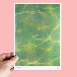 以下が含まれることがあります： 緑色の水面に反射する太陽光を捉えた写真の長方形のアートプリント。黄色い光の波紋模様が描かれています。下部の白い余白には、手書きの「30/30」という文字とイニシャルが記されています。