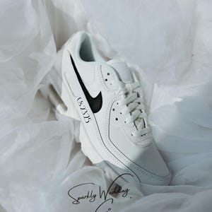 May include: White sneaker with a black swoosh and accents. The shoe has the text "CS 2325" on the side. The words "Sparkly Wedding Co." are written in cursive at the bottom.