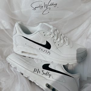 May include: White sneakers with black Nike swooshes and personalized text. One shoe reads "CS2325" and the other reads "Mr. Sully". The shoes are displayed on a white, textured surface, with the text "Sparkly Wedding Co." in the background.