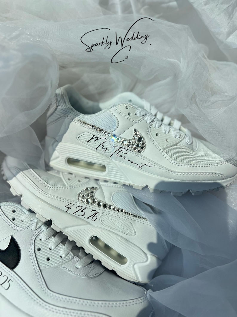 May include: White sneakers with crystal embellishments on the Nike swoosh and accents. The text "Mrs. Thorund" and the date "4.25.26" are written on the shoes. The shoes are part of the "Sparkly Wedding Co." collection.