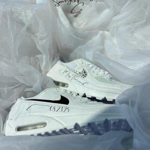 May include: White sneakers with black accents and the text "08.2325" and "Mrs. Thousand". The sneakers are displayed on a white, textured background with the text "Sparkly Wedding Co."