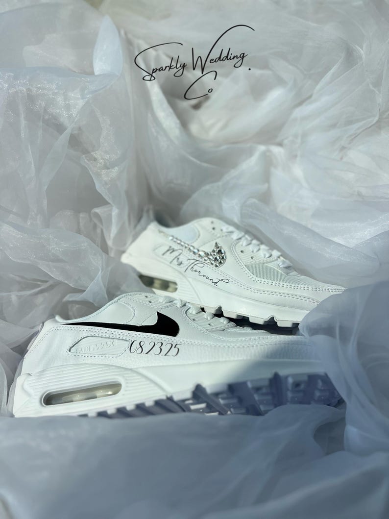 May include: White sneakers with black accents and the text "08.2325" and "Mrs. Thousand". The sneakers are displayed on a white, textured background with the text "Sparkly Wedding Co."