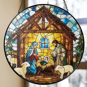 May include: Round stained glass window depicting the Nativity scene. The artwork features Mary, Joseph, and baby Jesus in a manger, surrounded by sheep. The scene is set in a stable with a wooden roof and a blue sky background. The window is framed in black.