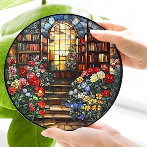 May include: A circular stained glass suncatcher featuring a detailed library scene with tall bookshelves, a central arched window, and a stone staircase surrounded by vibrant clusters of red, yellow, and blue flowers in a multi-colored glass design.