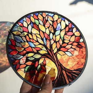 May include: A stained glass window featuring a colourful tree with leaves in shades of red, orange, yellow, green, blue, and purple. The tree is set against a background of orange and yellow.