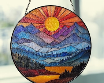May include: Round stained glass panel depicting a mountain landscape with a vibrant sunset. The sun is a bright yellow, with orange and red rays. The mountains transition from purple to blue. The panel is framed in black and hangs from a chain.
