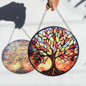 May include: A stained glass window hanging with a colorful tree of life design. The tree has a brown trunk and branches with leaves in shades of red, orange, yellow, green, and blue.