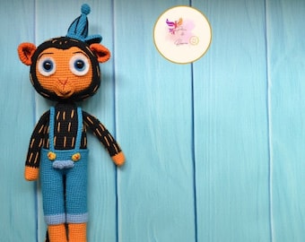 Op de afbeelding: Een gehaakt aapje met een blauwe muts en een overall. De aap heeft zwart haar, oranje handen en voeten en grote blauwe ogen.