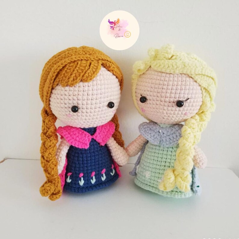 May include: Two crocheted dolls, one with brown hair and a blue dress with pink accents, and the other with blonde hair and a green dress with blue accents.