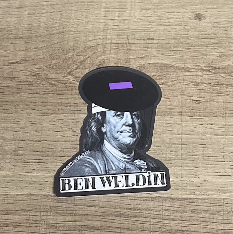 May include: A sticker featuring a black and white image of Benjamin Franklin wearing a welding mask. The text "BEN WELDIN" is printed in white block letters below the image. The welding mask has a purple lens.