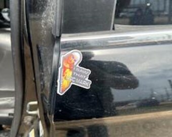 May include: A sticker with the text "RAW THAT PC MARK" and a graphic of a flame and a person. The sticker is affixed to the black door of a vehicle.