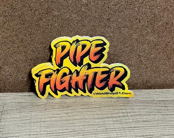 May include: A yellow sticker with the words "PIPE FIGHTER" in orange and black, with a brushstroke style. The sticker has a black border and the website address "WeldShop21.com" at the bottom.