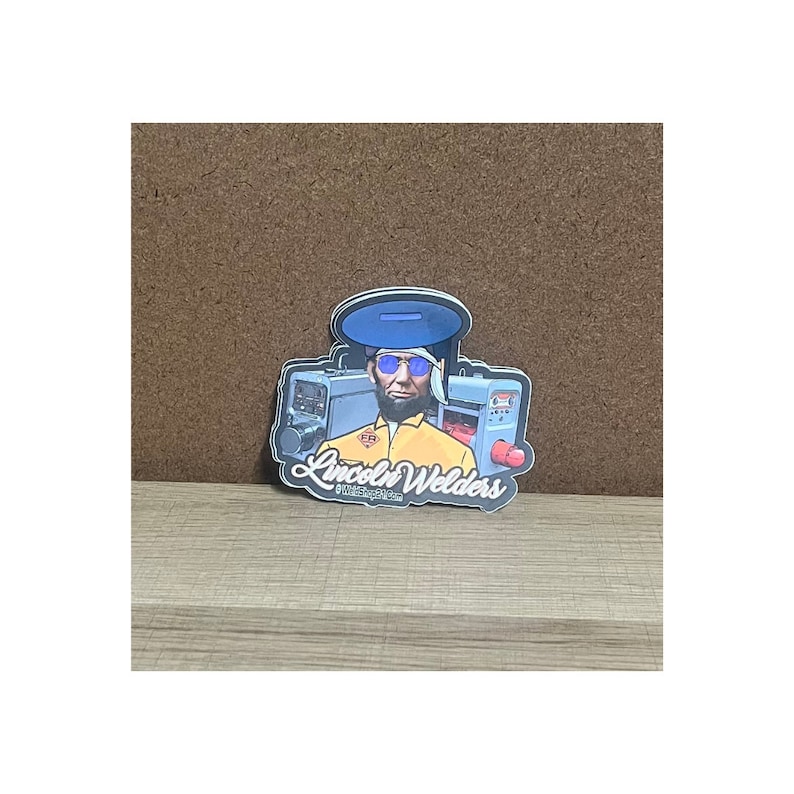 May include: A sticker featuring a cartoon illustration of a welder wearing blue sunglasses and a yellow jumpsuit, standing in front of welding equipment. The sticker has the text "Lincoln Welders" in a stylized font.