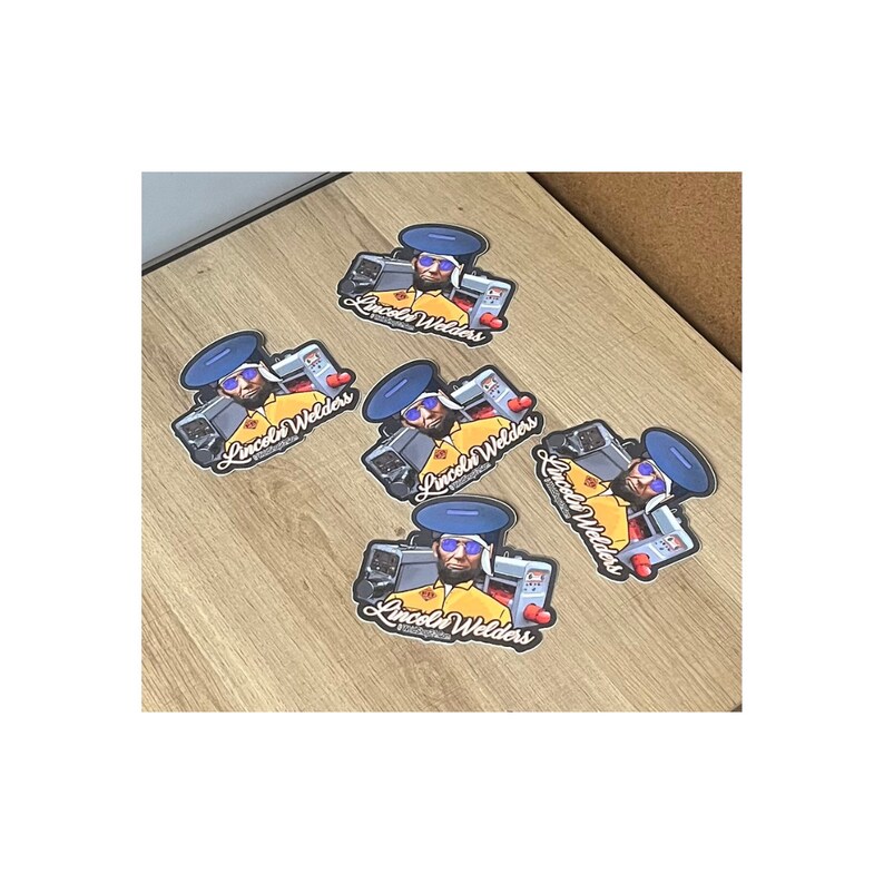 May include: Five colorful stickers featuring a cartoon illustration of a man wearing a blue hard hat and sunglasses, holding welding equipment. The stickers have the text "Lincoln Welders" in a stylized font.