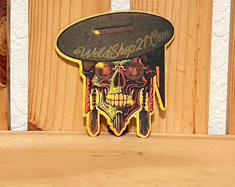 May include: A colorful sticker featuring a skull wearing sunglasses and a hat. The skull has a yellow and green design with orange accents. The hat is black with the text "WeldShop21.Com".