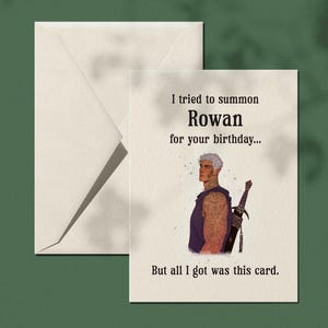 Peut inclure: Carte de vœux d'anniversaire avec l'illustration d'un homme avec une épée et le texte : "J'ai essayé d'invoquer Rowan pour votre anniversaire... Mais je n'ai eu que cette carte." La carte et l'enveloppe sont blanches, sur fond vert.