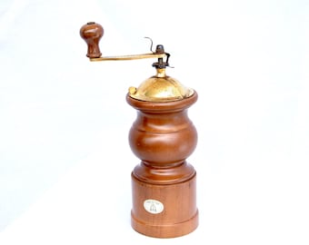 May include: A wooden pepper mill with a smooth, dark brown finish and a rounded, hourglass-shaped body. It features a polished brass top mechanism with a matching wooden crank handle and a small white oval sticker on the base with black text.