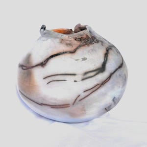 Könnte beinhalten: Handgefertigte Keramikvase mit einer einzigartigen, organischen Form. Die Vase hat eine weiße Basis mit dunklen, linearen Mustern und Akzenten in Braun und Orange. Die Öffnung ist unregelmäßig, was ihren künstlerischen Reiz verstärkt. Ein dekoratives Stück.
