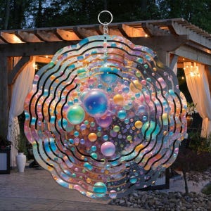 May include: A metal wind spinner with a circular design featuring multiple layers of swirling, iridescent bubbles in shades of blue, green, pink, and gold. The spinner is suspended from a silver hook.