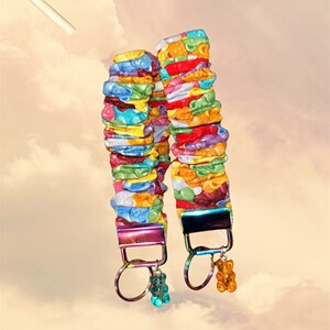 May include: Two colorful keychains with gummy bear patterns. Each keychain has a rainbow iridescent metal ring and a gummy bear charm.