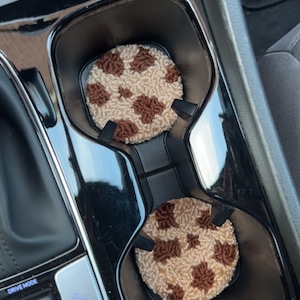 May include: Two brown and beige car cup coasters with a brown and white polka dot pattern. The coasters are in a car's cup holder.