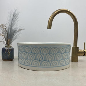 May include: A white ceramic sink with a blue and white geometric pattern. The sink is round and has a brass faucet.