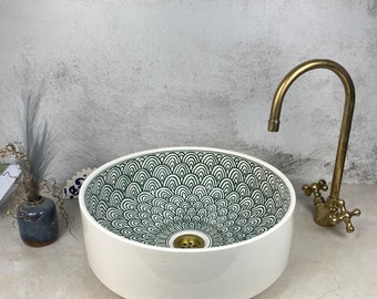 May include: A white ceramic sink with a green and white geometric pattern. The sink is round and has a single drain hole. A gold faucet is attached to the sink.