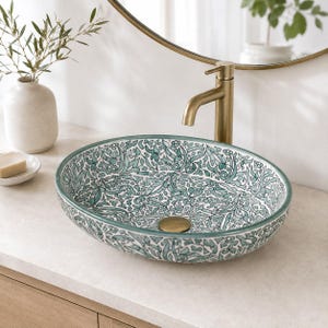 Peut inclure: Une vasque ovale en céramique ornée d'un motif floral détaillé bleu sarcelle et blanc sur ses surfaces intérieure et extérieure. Le lavabo comprend une bonde centrale dorée et est associé à un grand robinet en métal doré assorti.