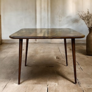 May include: A square wooden table with a natural wood grain finish and four slender legs. The table is made of dark wood and has a smooth, polished surface.