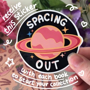 Image showing the freebie sticker that comes with each sticker book. It is a drawing of pink Saturn with the words "Spacing Out" surrounding it. The words "receive this sticker with each book to start your collection" are typed on the image