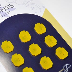 May include: Eight yellow resin buttons shaped like Lego minifigures with smiling faces. The buttons are arranged in a circle on a dark blue background.