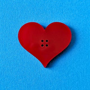May include: A red heart-shaped button with four black holes in the centre.