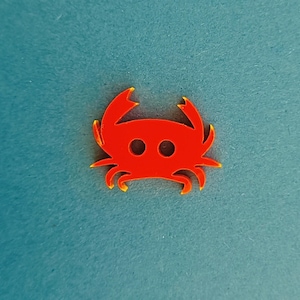 Può includere: Un ritaglio di granchio rosso con bordi gialli. Il granchio è un design semplice con due occhi e sei zampe.