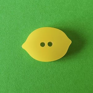 Può includere: Un bottone giallo a forma di limone con due fori.