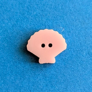 Può includere: Un bottone di plastica rosa a forma di conchiglia con due occhi neri.