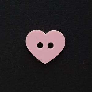 Puede incluir: Un botón de corazón rosa con dos agujeros.