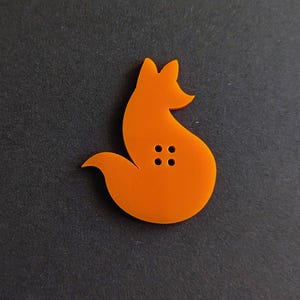 May include: Orange plastic button shaped like a fox sitting on its haunches. The button has four holes for sewing.