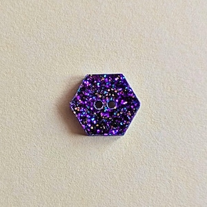 May include: A purple hexagonal button with a glittery finish and two holes in the centre.