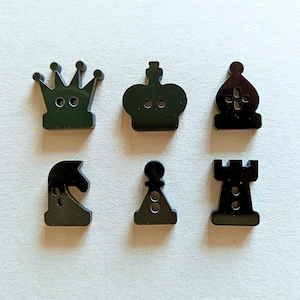 Può includere: Sei bottoni in plastica nera a forma di pezzi degli scacchi. I bottoni sono un re, una regina, un alfiere, un cavallo, una torre e un pedone.